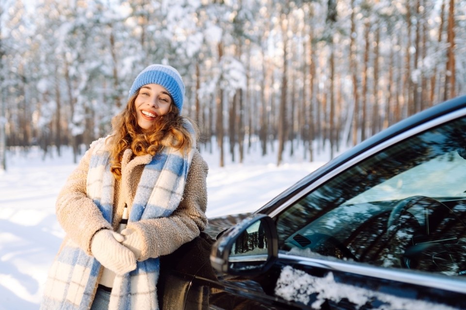 Rõõmus naine on ilusas talvises metsas oma uue autoga.