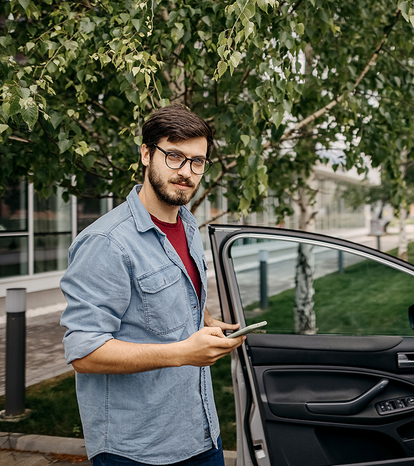 Young man standing next to a car and holding his phone.